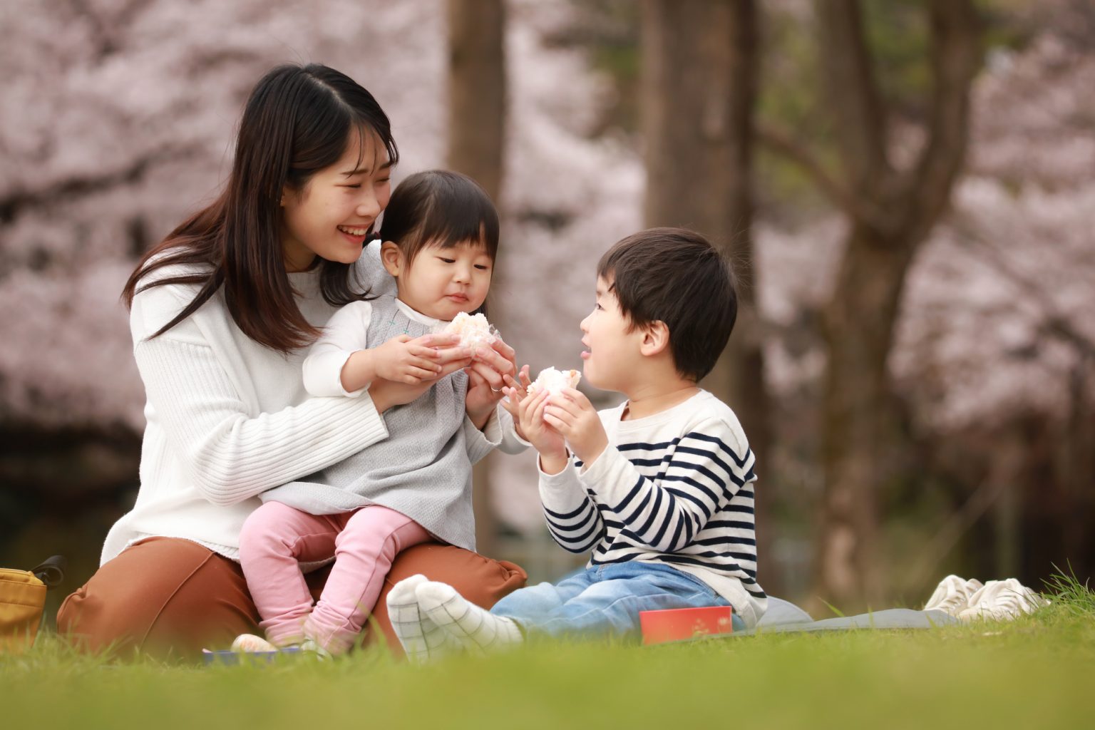 お母さんと子ども2人でおにぎりを食べるシーン