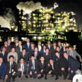 工場夜景をバックに船のデッキで記念写真をする会社員たち